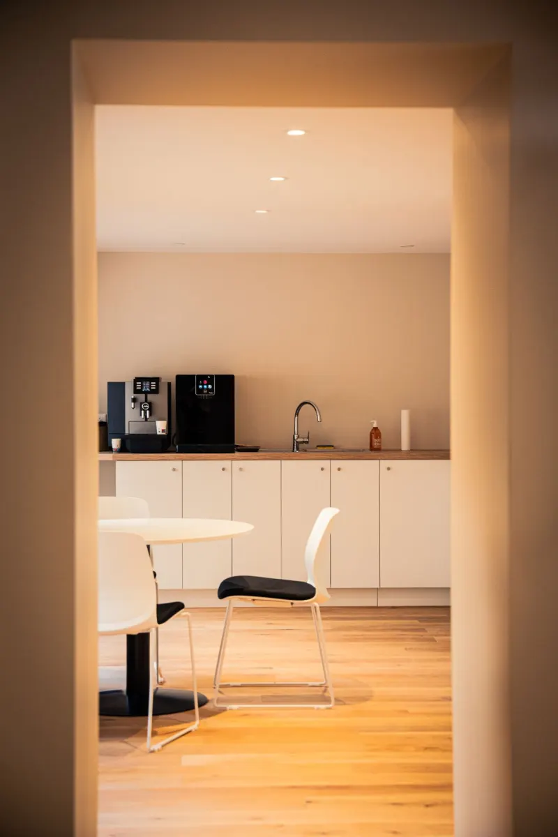 Kitchenette aménagée : meubles blancs et plan de travail en bois, vue par l'embrasure d'une porte