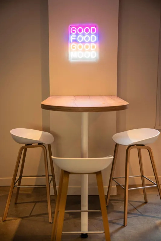 Mange-debout au plateau en bois et piètement blanc, entouré de trois tabourets hauts